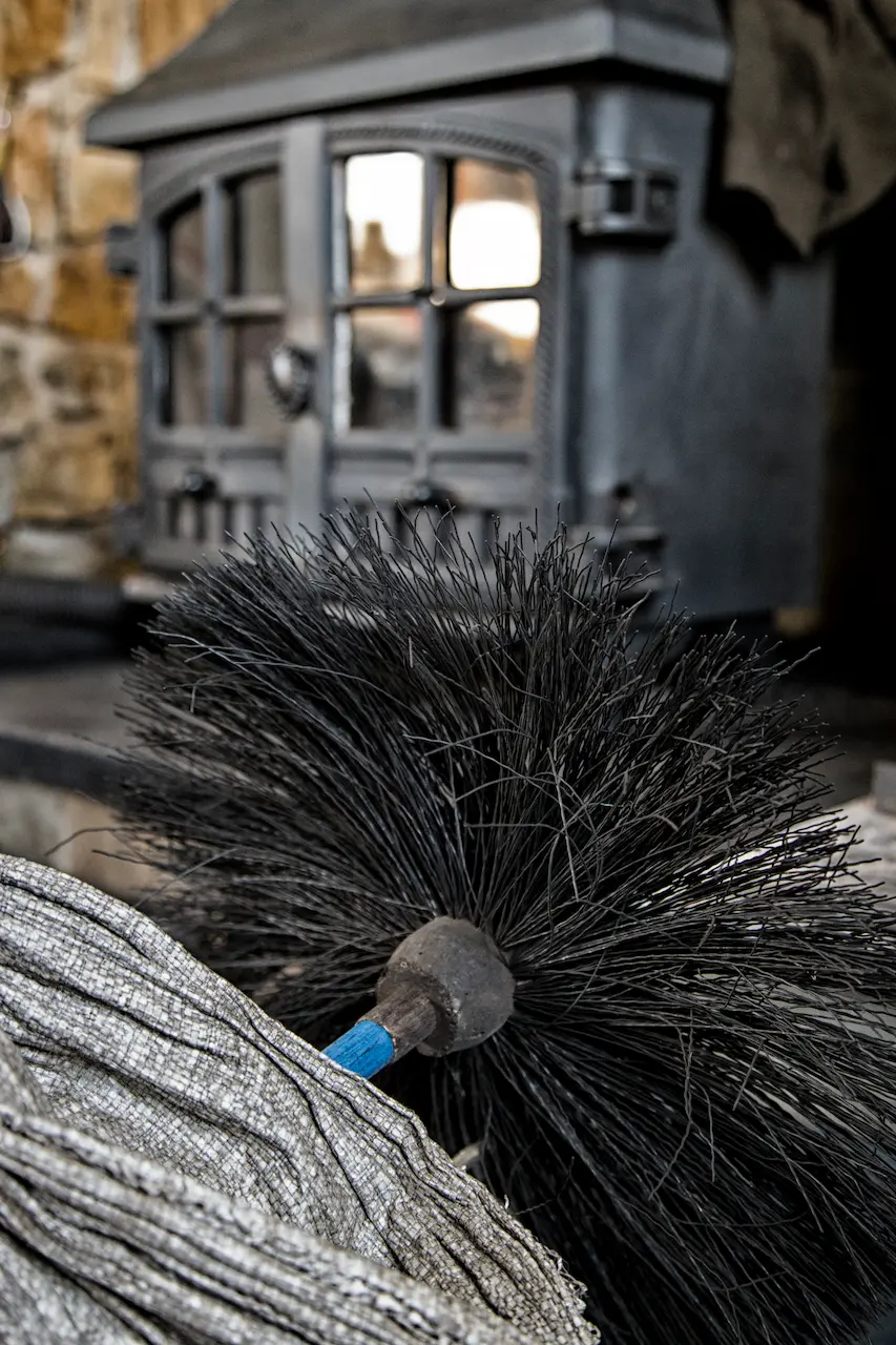 Chimney sweeping brush beside a wood-burning stove during professional maintenance