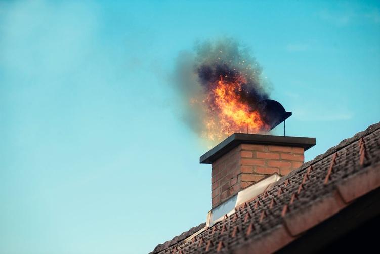 Dramatic chimney fire with flames and smoke erupting from brick chimney stack, demonstrating explosive dangers of blocked chimneys reaching temperatures over 2,000°F