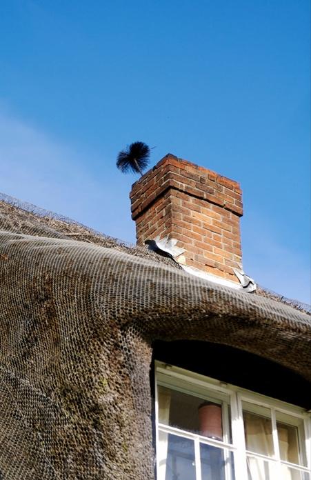 Professional chimney sweep brush protruding from brick chimney stack during cleaning process on thatched roof property, demonstrating active chimney maintenance service