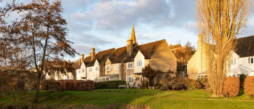 Traditional Cambridgeshire village houses with multiple chimney stacks reflected in river water during golden hour, showing typical properties requiring regular chimney maintenance