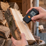 Digital pin-type moisture meter showing 18% while testing the freshly split face of firewood