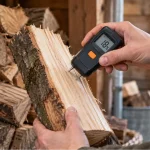 Digital pin-type moisture meter showing 18% while testing the freshly split face of firewood