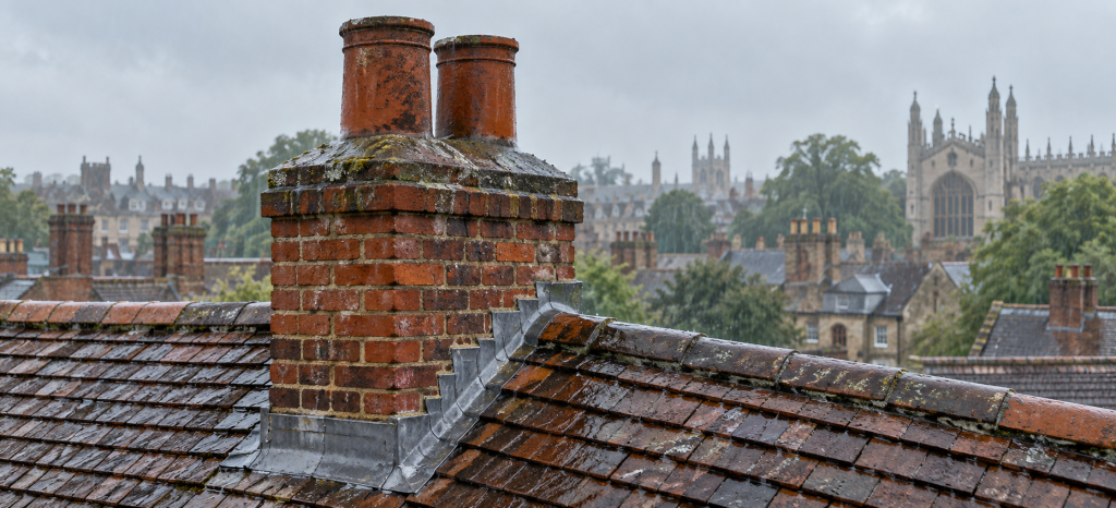 Rain falling on a traditional brick chimney stack and tiled roof, showing chimney pots, flaunching and lead flashing