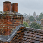 Rain falling on a traditional brick chimney stack and tiled roof, showing chimney pots, flaunching and lead flashing
