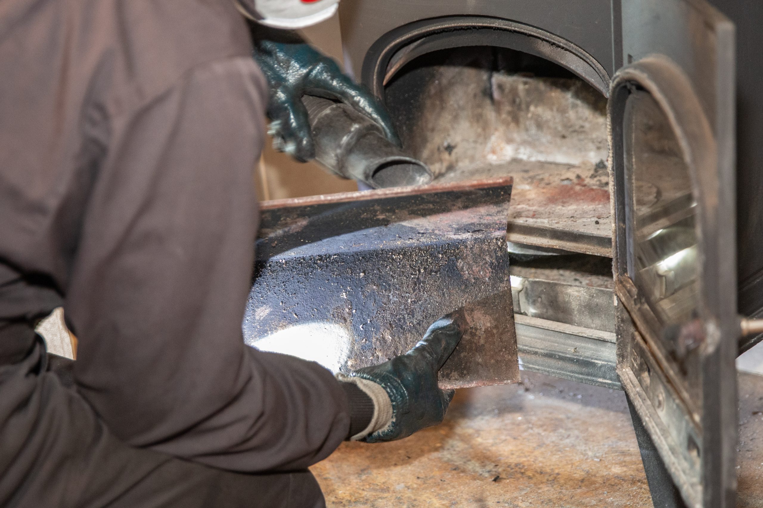 Chimney sweep removing the baffle plate from a wood-burning stove during maintenance