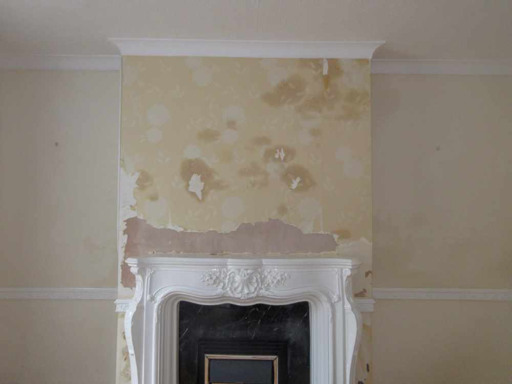 Brown damp staining on a chimney breast above a fireplace